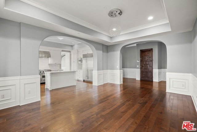 empty room with dark wood-type flooring, sink, a raised ceiling, and ornamental molding