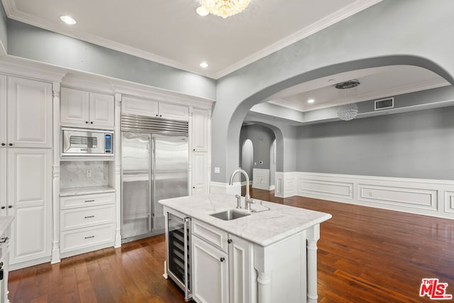 kitchen featuring white cabinetry, built in appliances, an island with sink, sink, and light stone counters