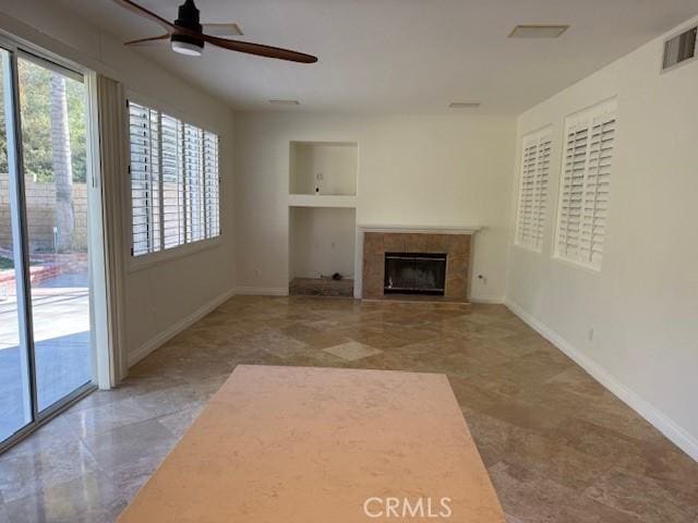 unfurnished living room featuring ceiling fan, a tiled fireplace, and built in features