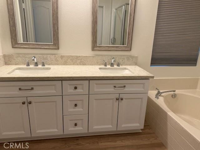 bathroom with a relaxing tiled tub, hardwood / wood-style flooring, and vanity