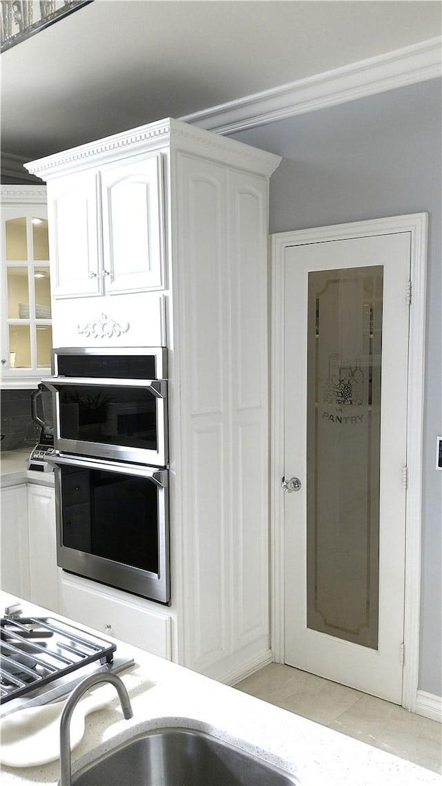 kitchen with white cabinets, double oven, light tile patterned flooring, and crown molding