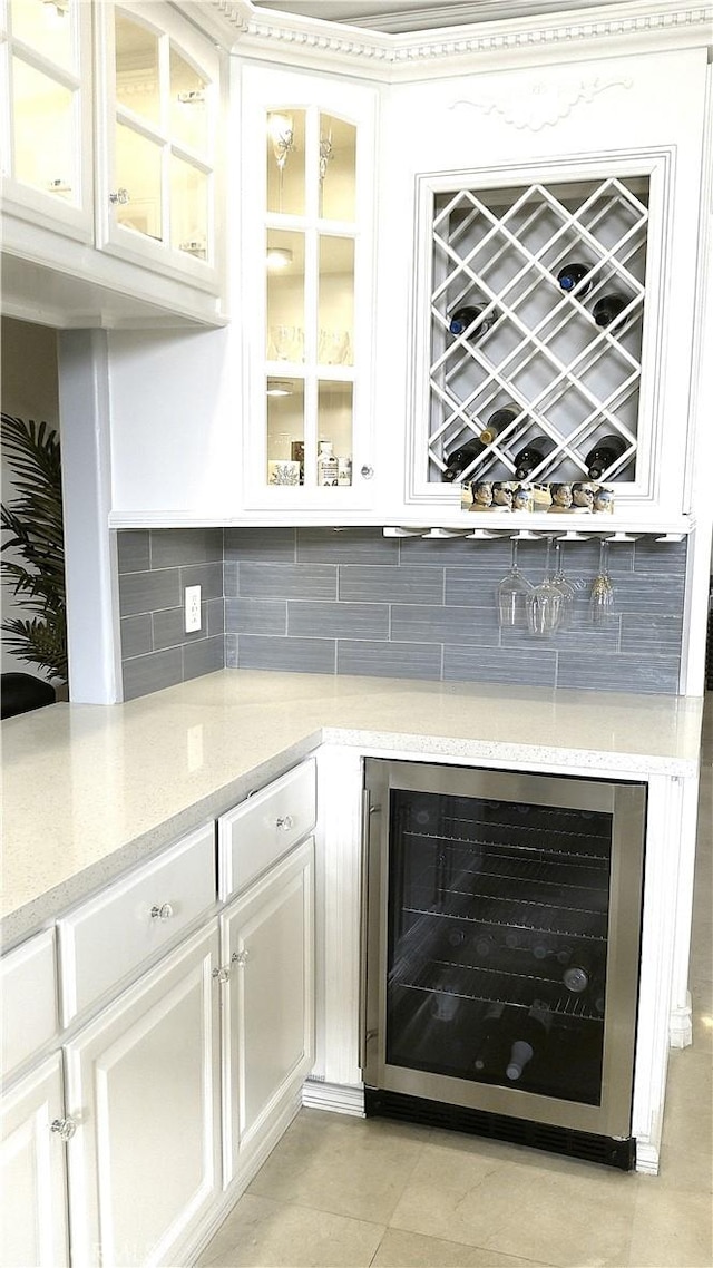 bar with light tile patterned floors, white cabinets, beverage cooler, and light stone countertops