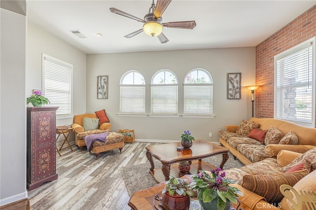 living room featuring ceiling fan, light hardwood / wood-style floors, brick wall, and a wealth of natural light