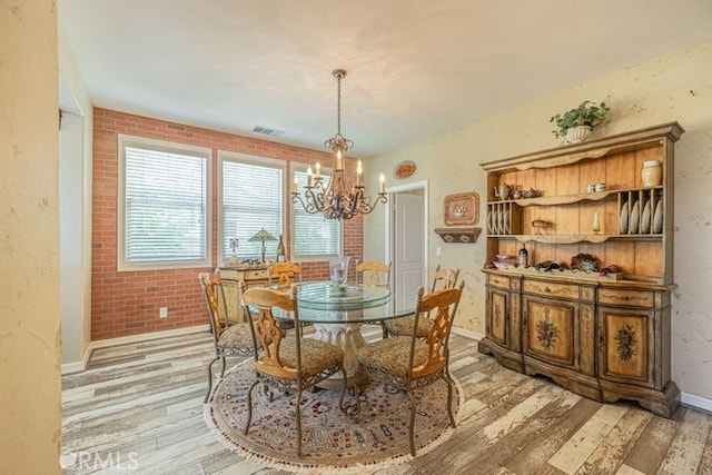 dining room with light hardwood / wood-style floors, brick wall, and an inviting chandelier