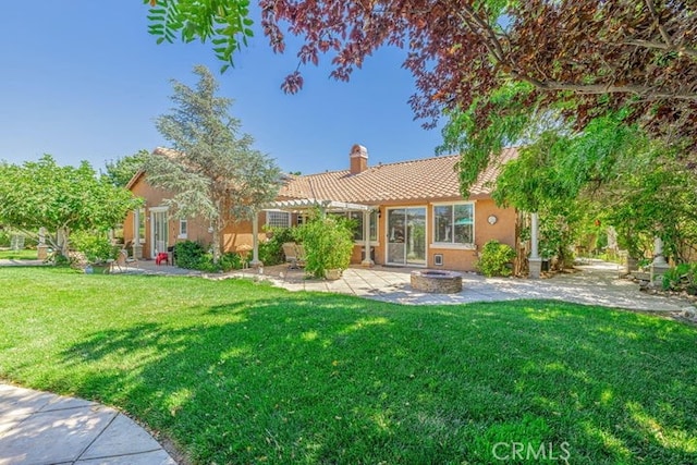 rear view of property featuring a yard, a patio area, and a fire pit