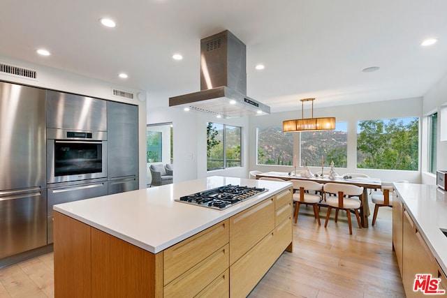 kitchen with decorative light fixtures, a kitchen island, island exhaust hood, light hardwood / wood-style flooring, and stainless steel gas cooktop