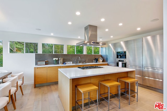 kitchen with a kitchen breakfast bar, island range hood, a large island, and appliances with stainless steel finishes