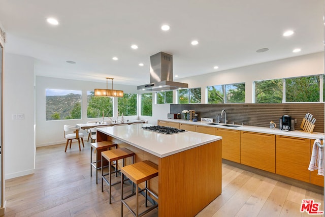 kitchen with stainless steel gas stovetop, a kitchen island, a kitchen bar, sink, and island range hood