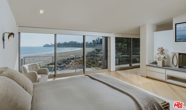 bedroom featuring light hardwood / wood-style floors, access to exterior, expansive windows, and a water view