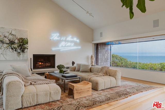 living room featuring a water view, wood-type flooring, track lighting, and high vaulted ceiling