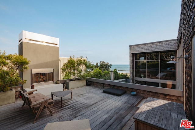 wooden terrace with exterior fireplace and a water view