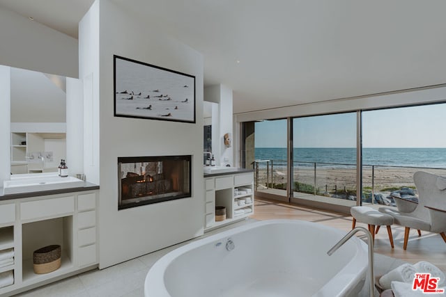 bathroom with tiled tub, built in shelves, vanity, a water view, and a view of the beach