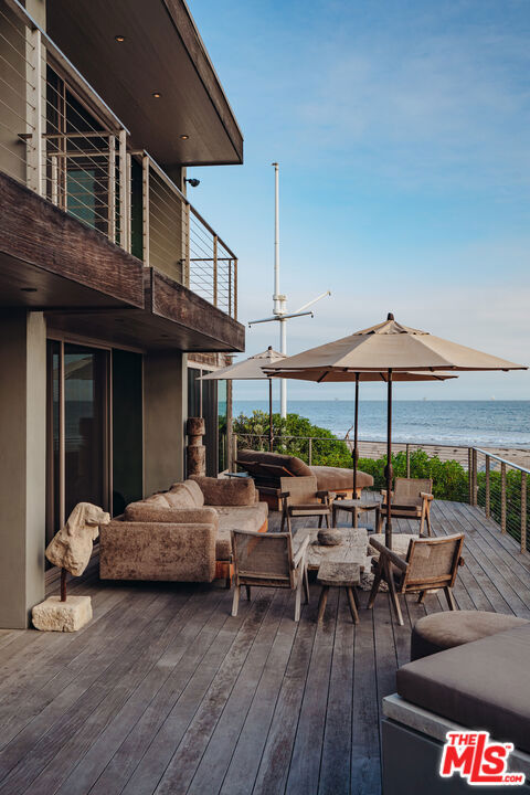 wooden terrace with an outdoor living space, a water view, and a view of the beach