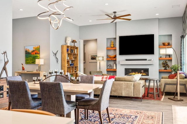 dining room with ceiling fan with notable chandelier, built in features, and light hardwood / wood-style flooring