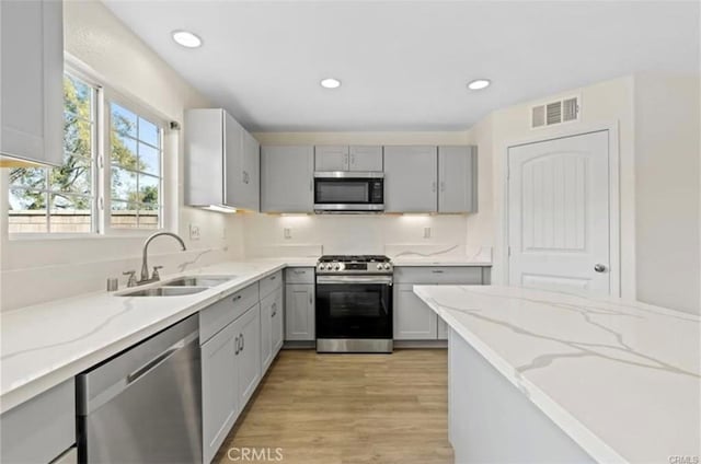 kitchen with gray cabinets, light stone counters, sink, and appliances with stainless steel finishes