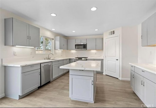 kitchen featuring appliances with stainless steel finishes, sink, gray cabinetry, a center island, and light hardwood / wood-style floors