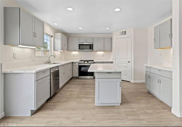 kitchen with appliances with stainless steel finishes, light wood-type flooring, sink, a center island, and gray cabinets