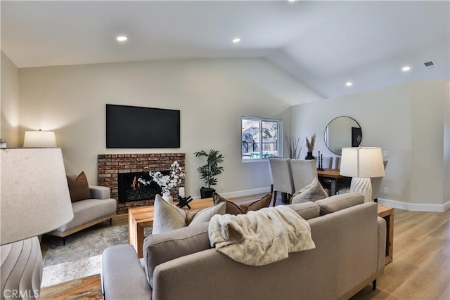 living room with vaulted ceiling, light wood-type flooring, and a fireplace