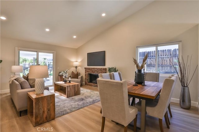 dining area with a brick fireplace, light hardwood / wood-style floors, and high vaulted ceiling