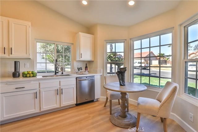 kitchen featuring white cabinets, vaulted ceiling, stainless steel dishwasher, light hardwood / wood-style flooring, and sink