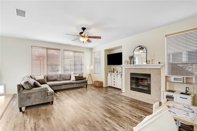 living room featuring light wood-type flooring, ceiling fan, and a tiled fireplace