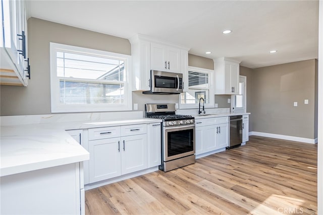 kitchen featuring white cabinetry, appliances with stainless steel finishes, light wood-type flooring, light stone counters, and sink