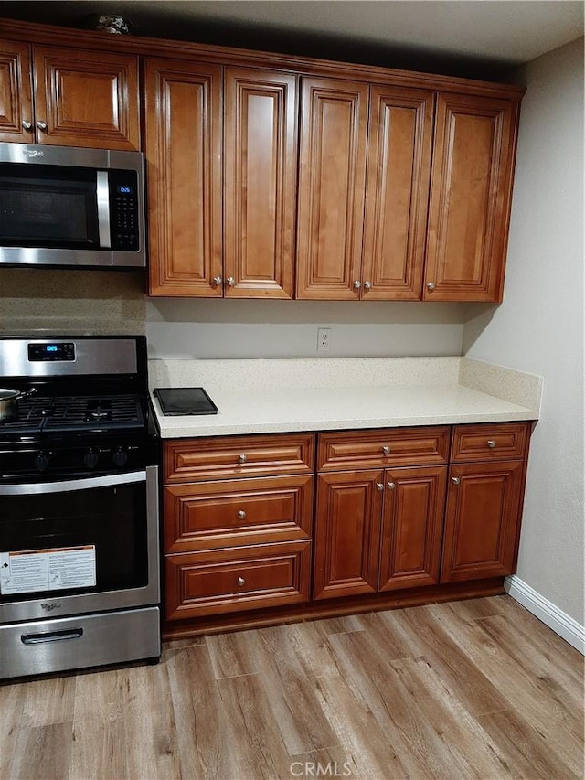 kitchen featuring light countertops, appliances with stainless steel finishes, brown cabinetry, and light wood-style flooring