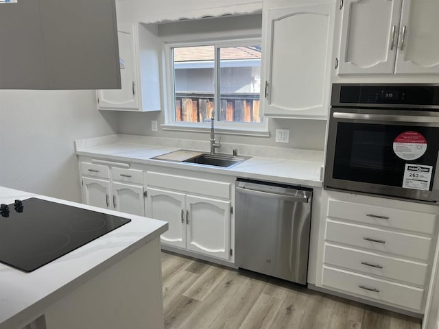 kitchen with appliances with stainless steel finishes, light hardwood / wood-style floors, white cabinetry, and sink