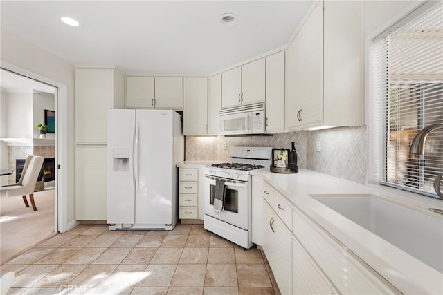 kitchen featuring white appliances, a wealth of natural light, white cabinets, backsplash, and sink