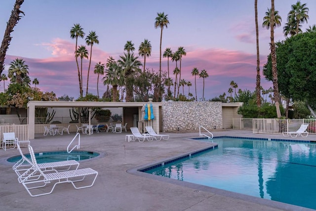 pool at dusk featuring a patio area and a hot tub