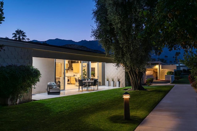 back house at dusk with a patio area, a mountain view, and a yard