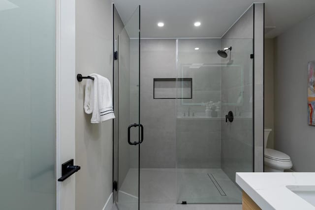 bathroom featuring toilet, vanity, and a shower with door