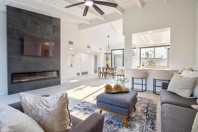 living room with ceiling fan with notable chandelier, high vaulted ceiling, beamed ceiling, and a fireplace