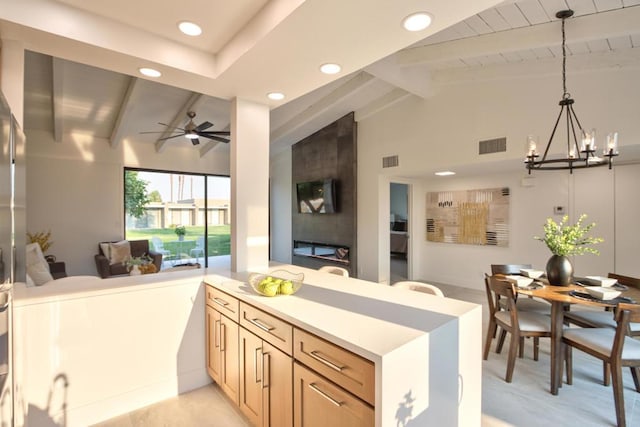 kitchen featuring ceiling fan with notable chandelier, vaulted ceiling with beams, light brown cabinetry, hanging light fixtures, and kitchen peninsula