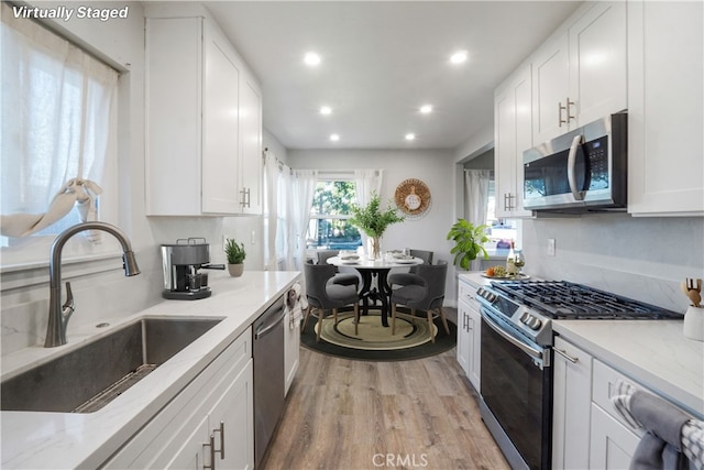 kitchen with white cabinetry, sink, light stone countertops, and appliances with stainless steel finishes