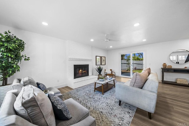 living room with ceiling fan, a brick fireplace, and hardwood / wood-style flooring