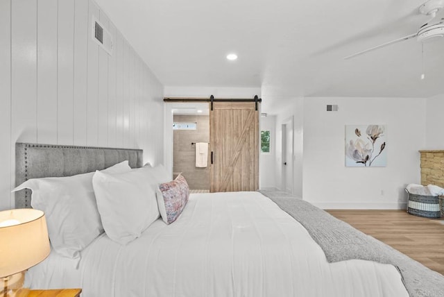 bedroom featuring wood walls, ceiling fan, a barn door, and wood-type flooring