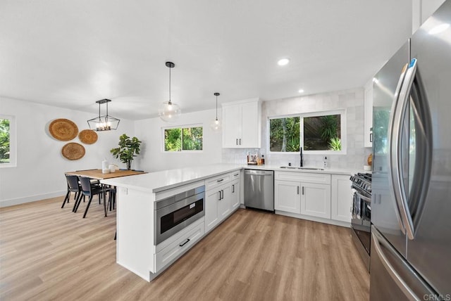 kitchen featuring white cabinetry, stainless steel appliances, decorative backsplash, hanging light fixtures, and kitchen peninsula