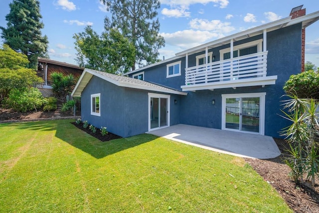 rear view of house featuring a lawn, a balcony, and a patio