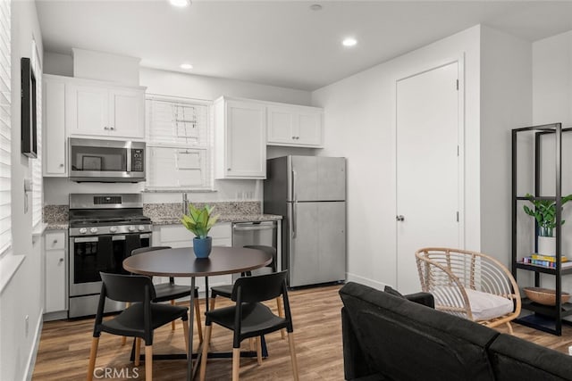 kitchen featuring white cabinets, appliances with stainless steel finishes, light stone counters, and light hardwood / wood-style floors