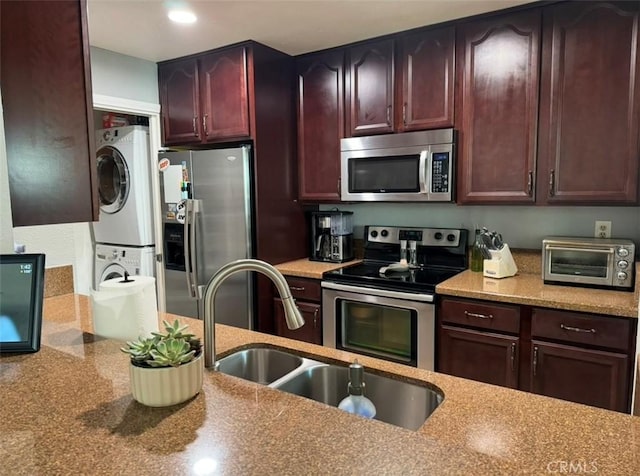 kitchen featuring light stone countertops, stacked washing maching and dryer, appliances with stainless steel finishes, and sink