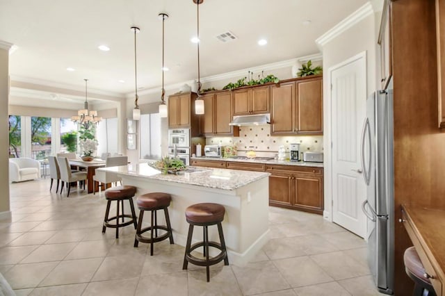 kitchen featuring appliances with stainless steel finishes, a kitchen island with sink, hanging light fixtures, a kitchen breakfast bar, and light stone countertops