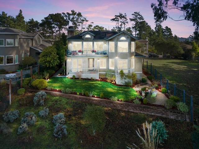 back house at dusk with a balcony and a yard