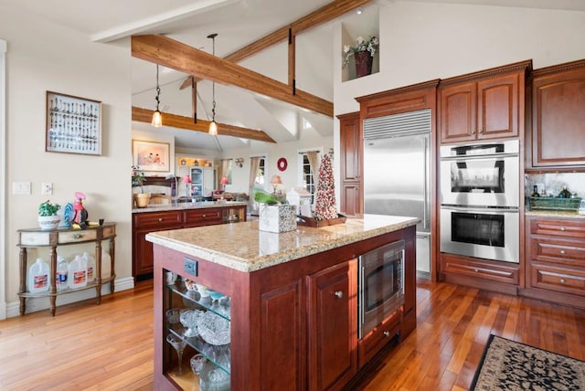 kitchen with beamed ceiling, built in appliances, decorative light fixtures, a kitchen island, and hardwood / wood-style flooring