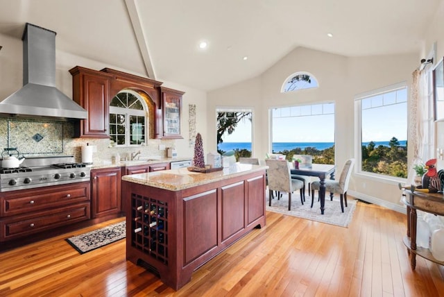 kitchen featuring wall chimney range hood, light hardwood / wood-style flooring, a center island, a water view, and stainless steel gas stovetop