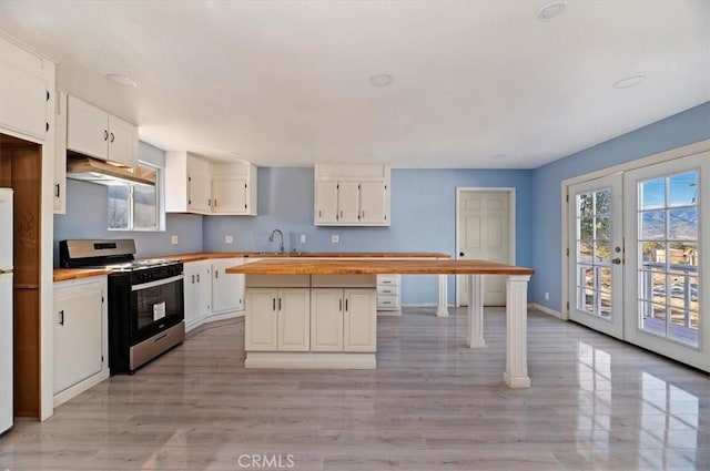 kitchen with a center island, stainless steel stove, white cabinetry, french doors, and wood counters