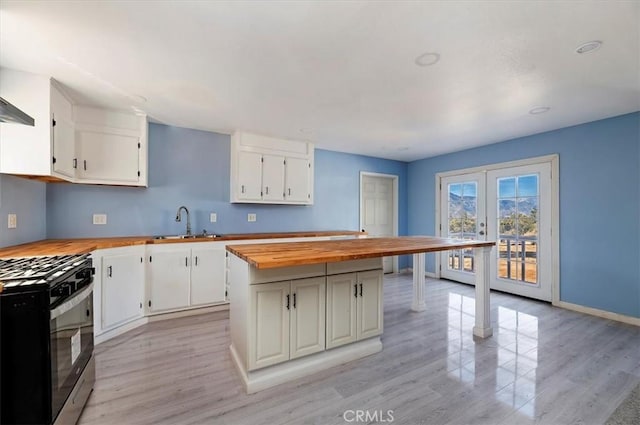 kitchen featuring butcher block countertops, stainless steel range with gas stovetop, light hardwood / wood-style floors, sink, and white cabinets