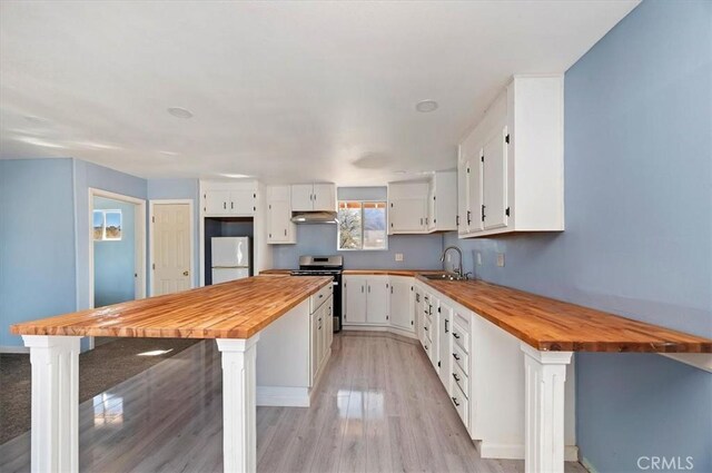 kitchen with white cabinetry, stainless steel stove, butcher block counters, and white fridge