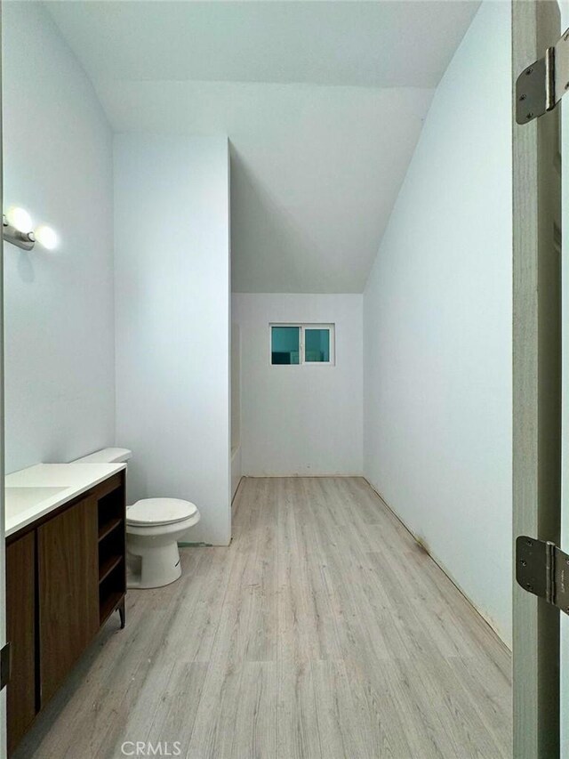 bathroom with toilet, vanity, wood-type flooring, and lofted ceiling