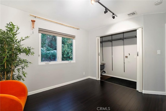 unfurnished bedroom with rail lighting, ensuite bathroom, dark hardwood / wood-style flooring, and a closet